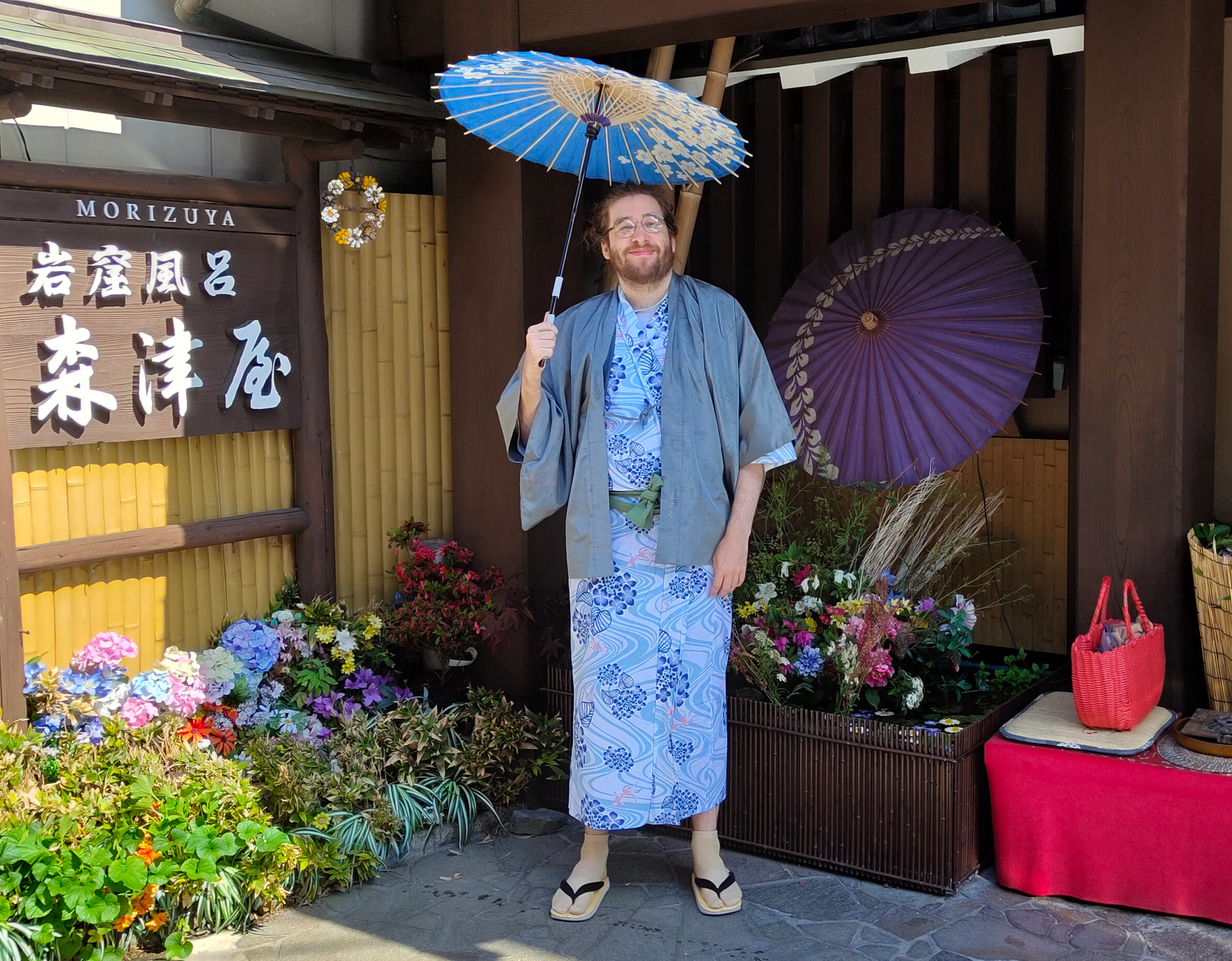 Craig standing outside a traditional wooden building in Japan holding a blue paper umbrella